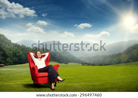 smiley young woman resting in red chair on the green meadow over beautiful landscape with hills, forest and sky