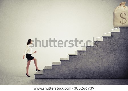 smiley businesswoman rising up stairs and looking at big bag with money on the top over grey background