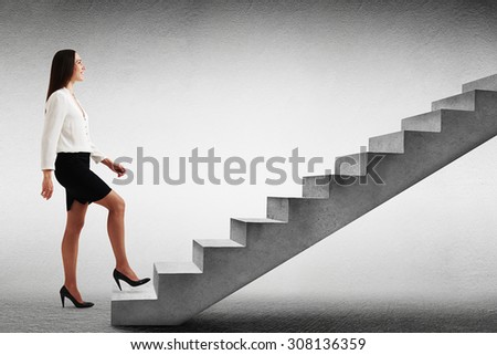 smiley businesswoman in formal wear walking up concrete stairs over light grey background