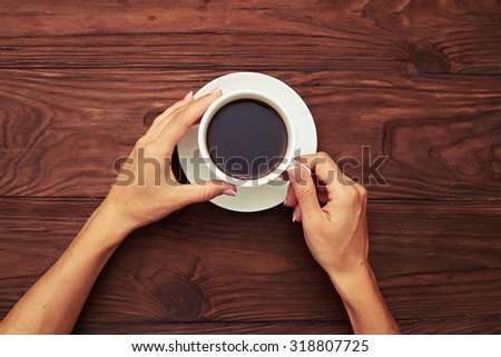 view from above on womans hands holding cup of coffee over wooden table