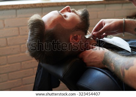 barber shaving man with vintage straight razor in barbershop