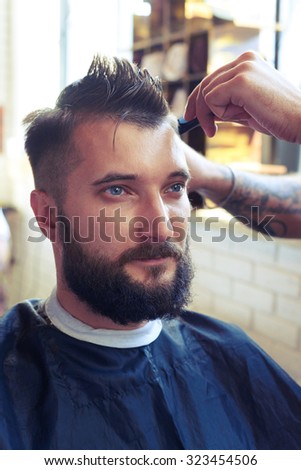 portrait of handsome man with beard in barber shop. barber cutting hair with scissors and comb