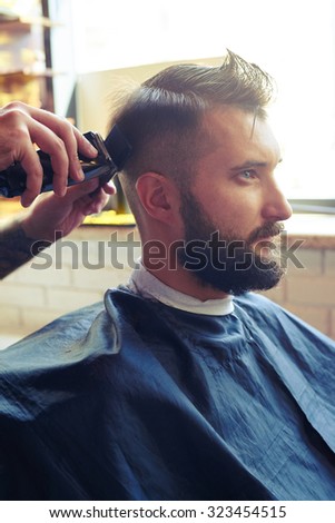 sideview portrait of handsome man in a barber shop. barber cutting hair with electric clipper and comb