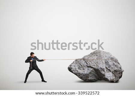 businessman in formal wear pulling the big stone over light grey background