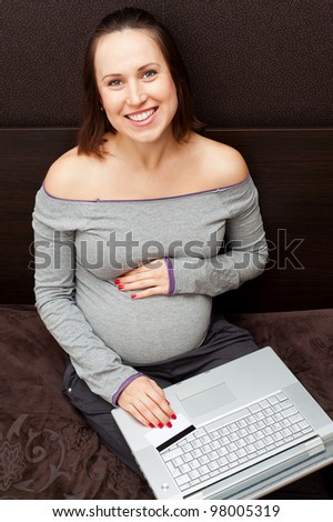 smiley pregnant woman with laptop and credit card at home