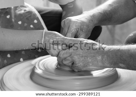 A potters hands guiding a child hands to help him to work