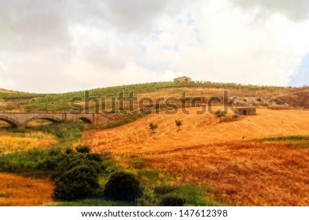 Idyllic Sicilian Summer Landscape with old huts, an old aqueduct like railway and a man, working in the fields