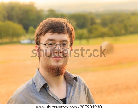 Bearded young caucasian man with glasses in a high summer corn field