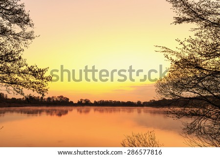 Serene Sunrise at the Lake. Spring Dawn. Lovely colors. Tree Silhouettes and warm water in Bavaria, Germany
