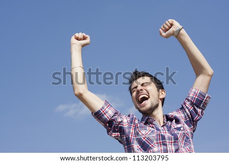 Portrait of happy young man raising his hands with cloudy sky above him