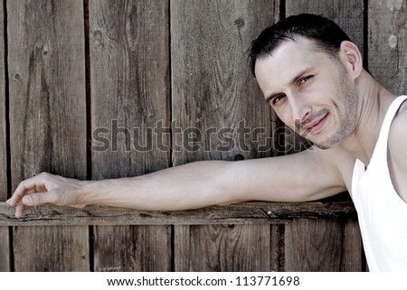 Happy young man leaning against a fence and smiling