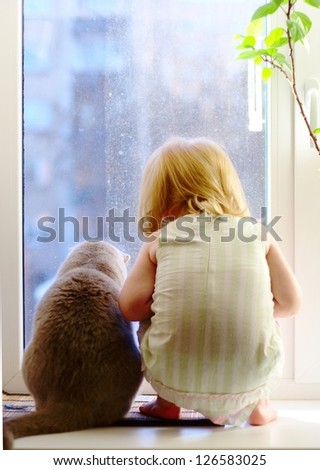 Best friends. Cat and little girl looking out of the window.