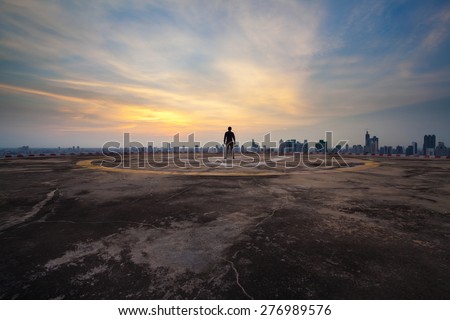 A man standing on the concrete floor of skyscraper rooftop building watch a city sunset
