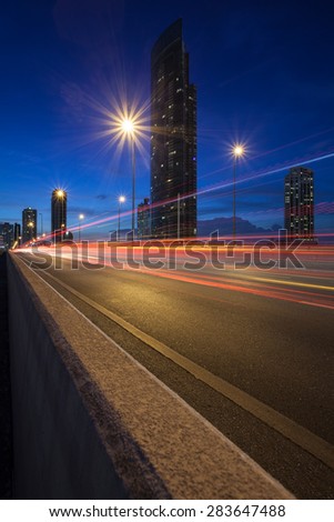 Highway road with light trails and modern building on background in Bangkok city at dusk