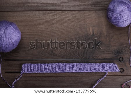 knitting needles and balls of threads over wooden background
