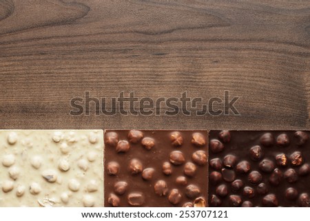 black, milk and white chocolate bars with whole hazelnuts on wooden table