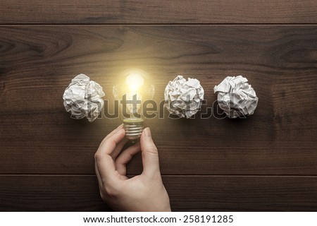new idea concept with crumpled office paper, female hand holding light bulb