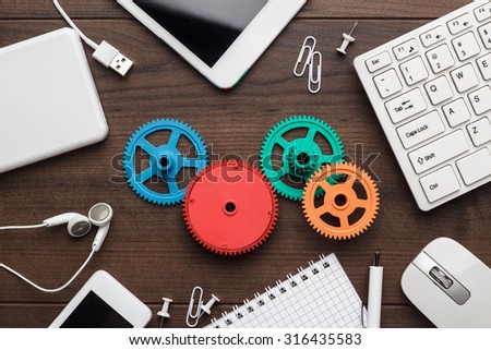 workflow and teamwork concepts with colorful gears different gadgets and office stationery on the wooden table