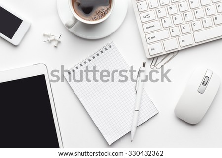 overhead of white office table with notebook, computer keyboard and mouse, tablet pc and smartphone