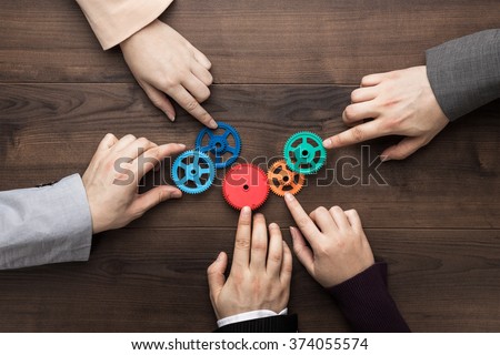 Teamwork concept. Different hands of men and women connect colorful gears into working mechanism on the brown wooden table background. Each has its own role in problem-solving. Experience exchange