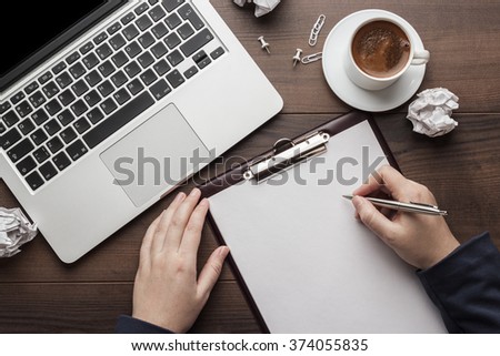 view from above businesswoman writing. brown wooden office table with cup of coffee, notepad and laptop computer
