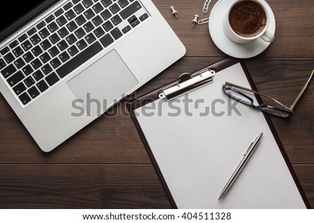view from above. brown wooden office table with cup of coffee, notepad and laptop computer