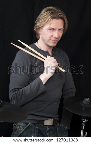Standing man in front of a black background an his drums is holding drumsticks