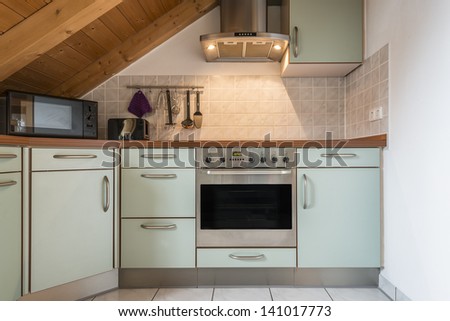 kitchen of a flat with oven, microwave, stove, hood, cabinets and wooden ceiling