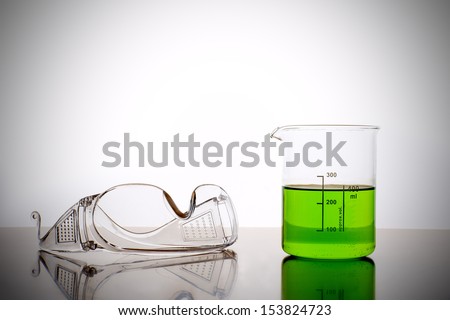 Measuring glass with green liquid and safety glasses, goggles in a chemical lab