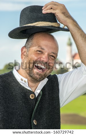 Portrait of a laughing man in traditional bavarian clothes with monastery Andechs in Bavaria, Germany