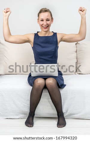 Picture of a happy woman sitting on sofa with laptop and holding arms up