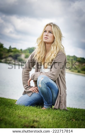 Blond woman kneeling on a green meadow at the edge of a lake in summer
