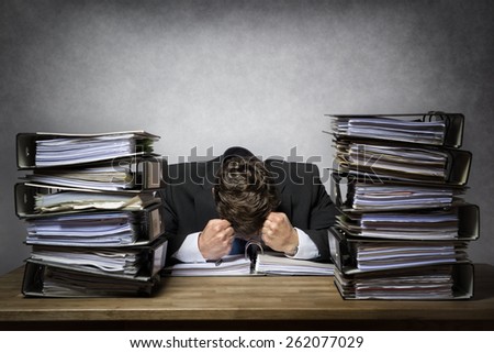 Overworked frustrated businessman with lot of files on his desk