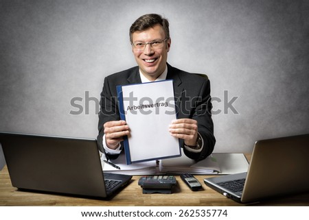 Businessman at the office desk holds a file with german text Arbeitsvertrag (in english employment agreement)