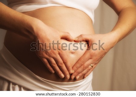 Close up of a baby bump with holding hands like a heart