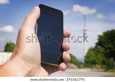 Image of hand with mobile phone and broadcasting tower in the background