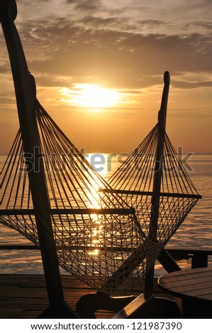 a hammock on a wooden platform by the sea looks inviting against a beautiful golden sunset