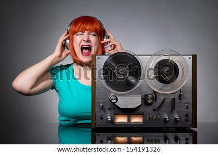 Woman in headphones with a retro reel audio tape recorder on dark background