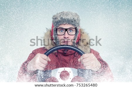 Happy man in winter clothes with a steering wheel, snow blizzard. Concept car driver