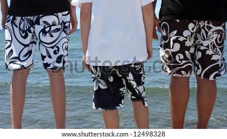 Three teenage boys in swim suits ready to jump into the water.