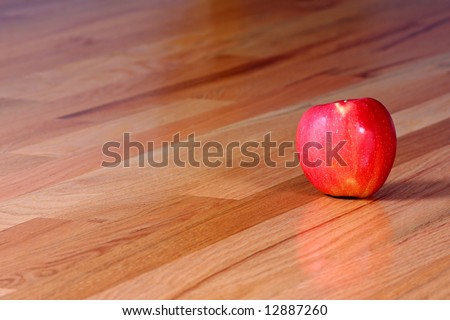 A shiny red apple on a hardwood floor.