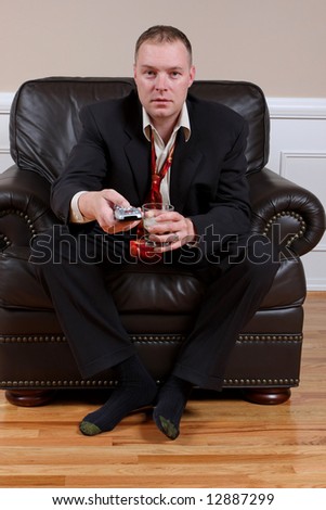 A man with a TV remote control and a drink captivated by what is on television.