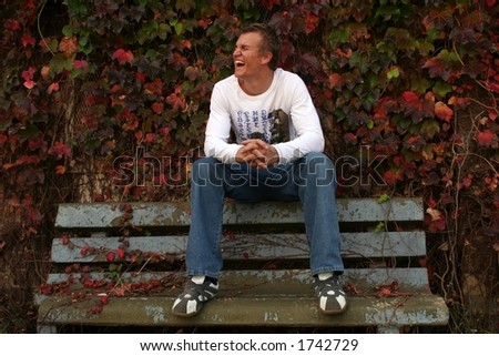Young man on a park bench laughing.