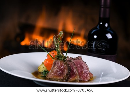 Lamb chops with vegetables and a bottle of wine in front of a fireplace