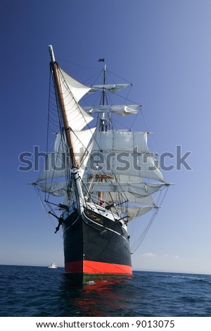 Tall Sailing Ship at Sea under full sail with tall ships in the background.