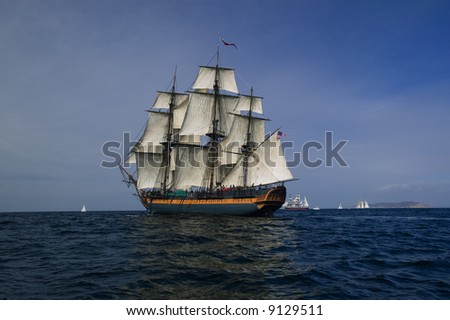 Vintage Frigate Sailing Ship at Sea under full sail with tall ships in the background.