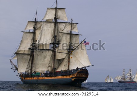 Vintage Frigate Sailing Ship at Sea under full sail with tall ships in the background.