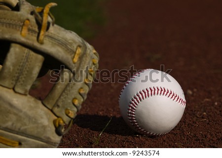 Baseball in a mit sitting on the grass and dirt of a diamond