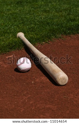 Baseball and bat on the on the dirt and grass of a ball field