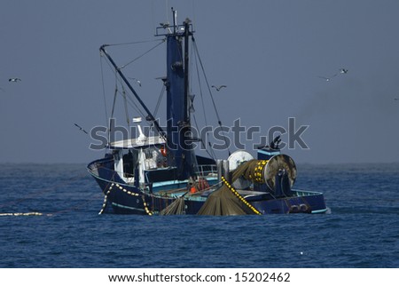 Fishing boat with nets deployed and sea gulls flying overhead